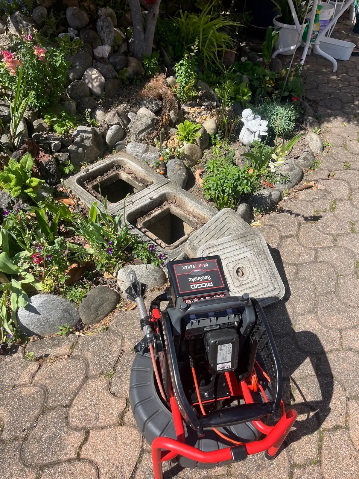 Enrouleur de caméra d’inspection installé près de deux regards ouverts dans un jardin